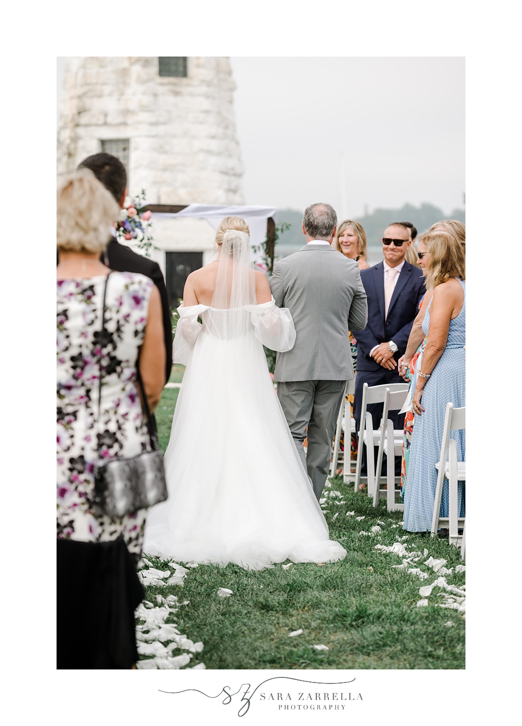 bride walks down aisle on dad's arm for ceremony in front of Newport Lighthouse 