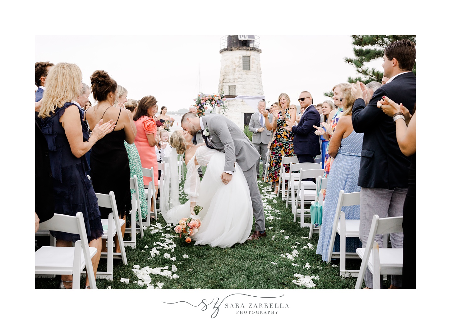 groom dips bride in aisle after wedding ceremony on lawn in front of Newport Lighthouse 