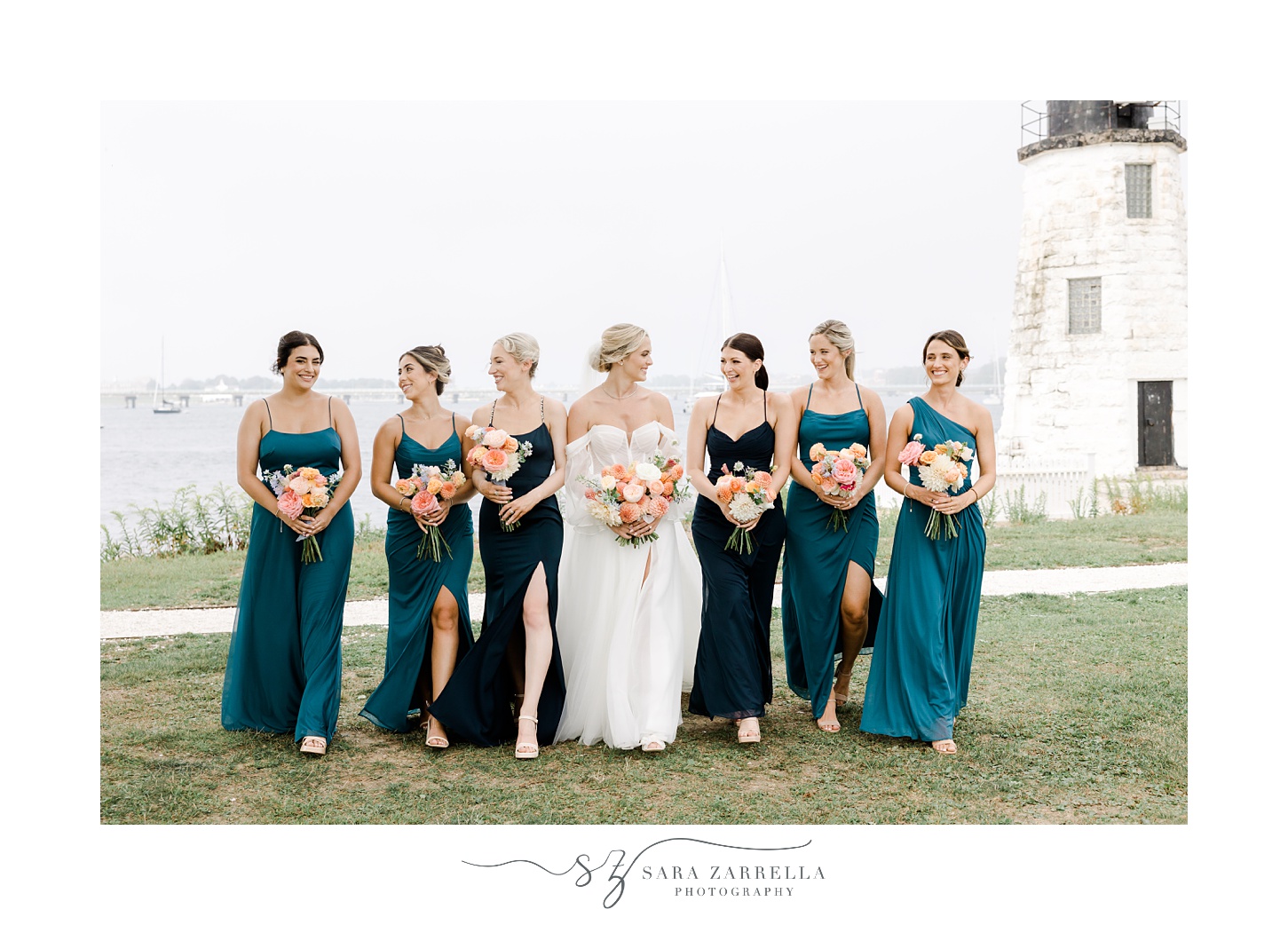 bride and bridesmaids in teal gowns walk across lawn in front of Narragansett Bay