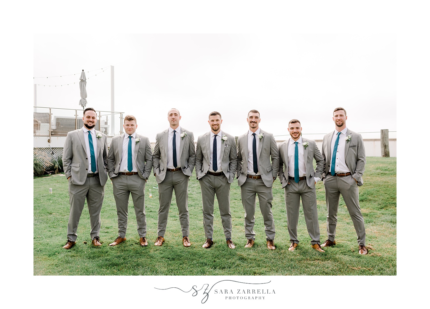groom and groomsmen stand with hands in pocket of grey suits at Narragansett Bay