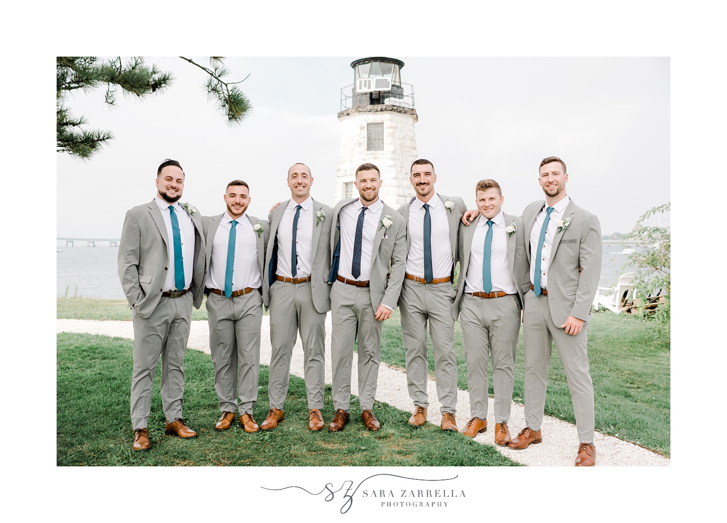 groom stands with groomsmen in grey suits in front Newport Lighthouse 