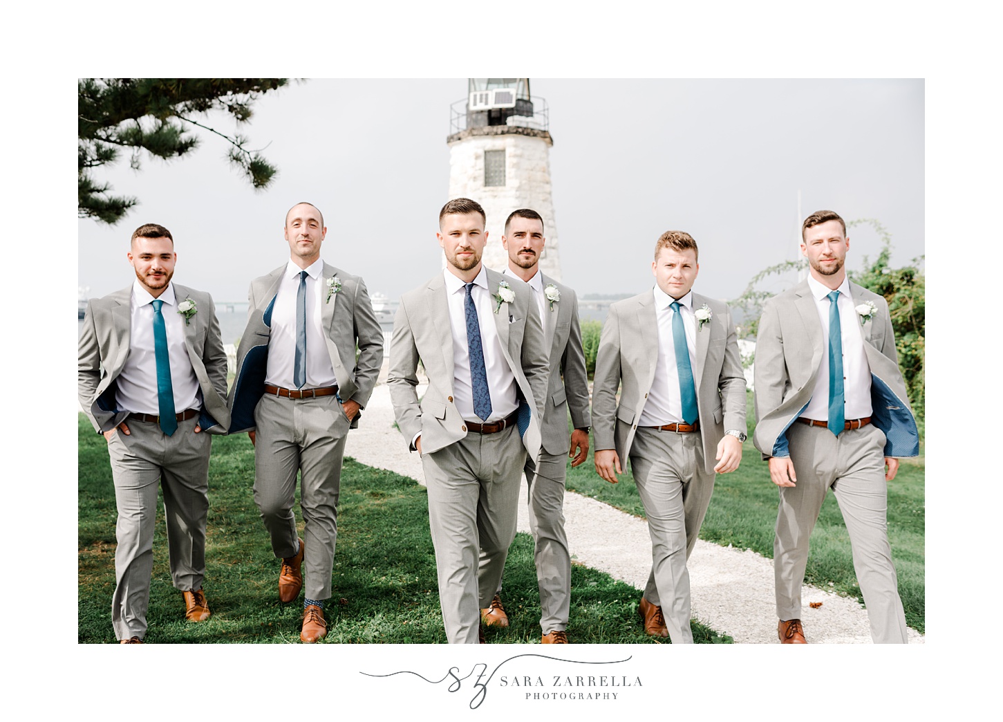 groom and groomsmen in grey suits walk near Newport Lighthouse 