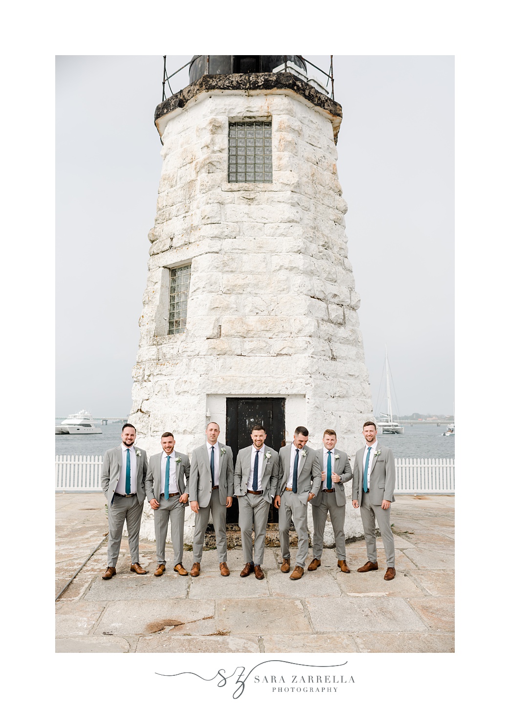 groom and groomsmen in grey suits pose in front of Newport Lighthouse 