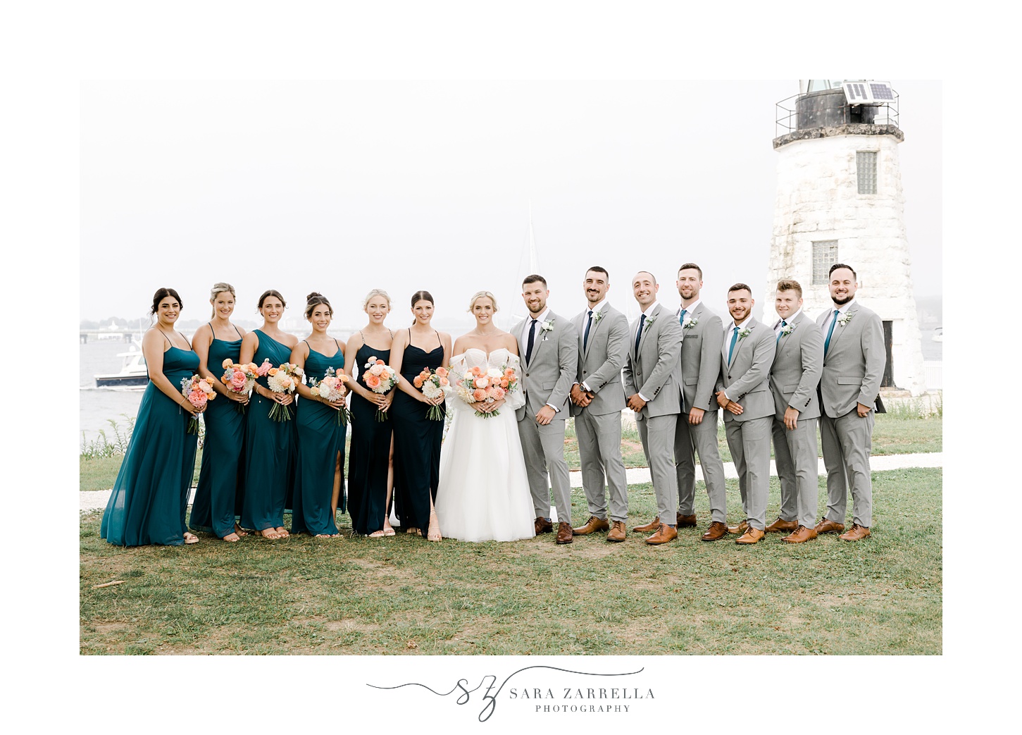 bride and groom stand with wedding party in a line in front of Narragansett Bay