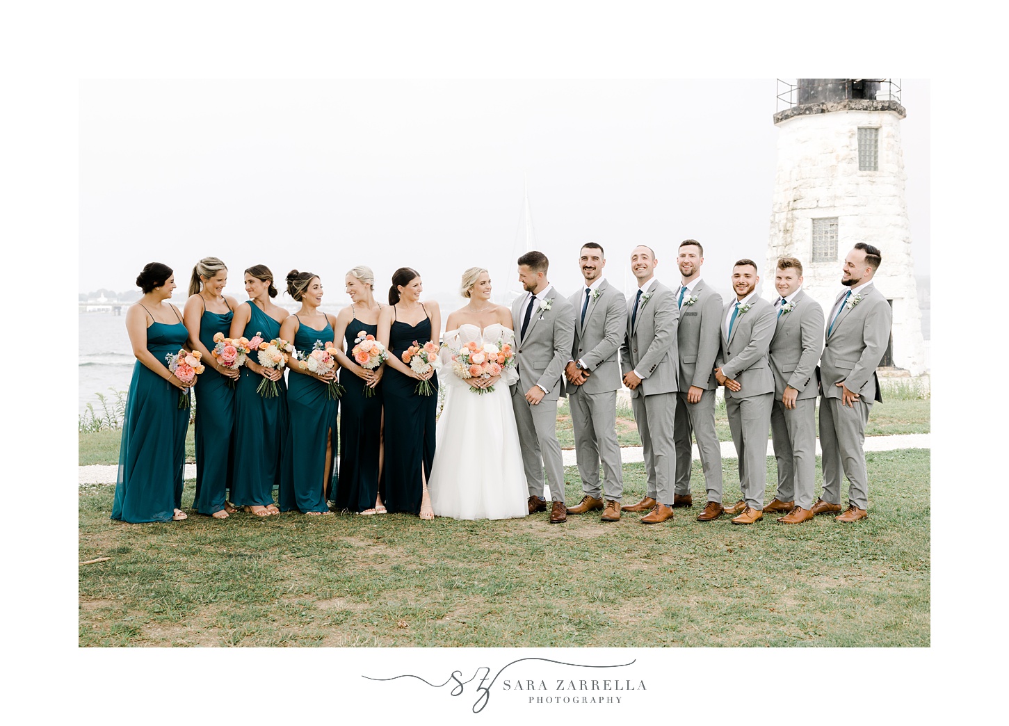 bride and groom stand with wedding party in a line in front of Narragansett Bay