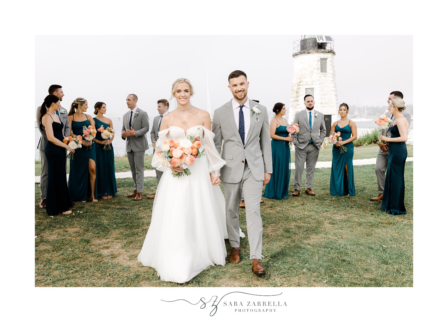 bride and groom walk with wedding party behind them in front of Narragansett Bay at Newport Lighthouse 