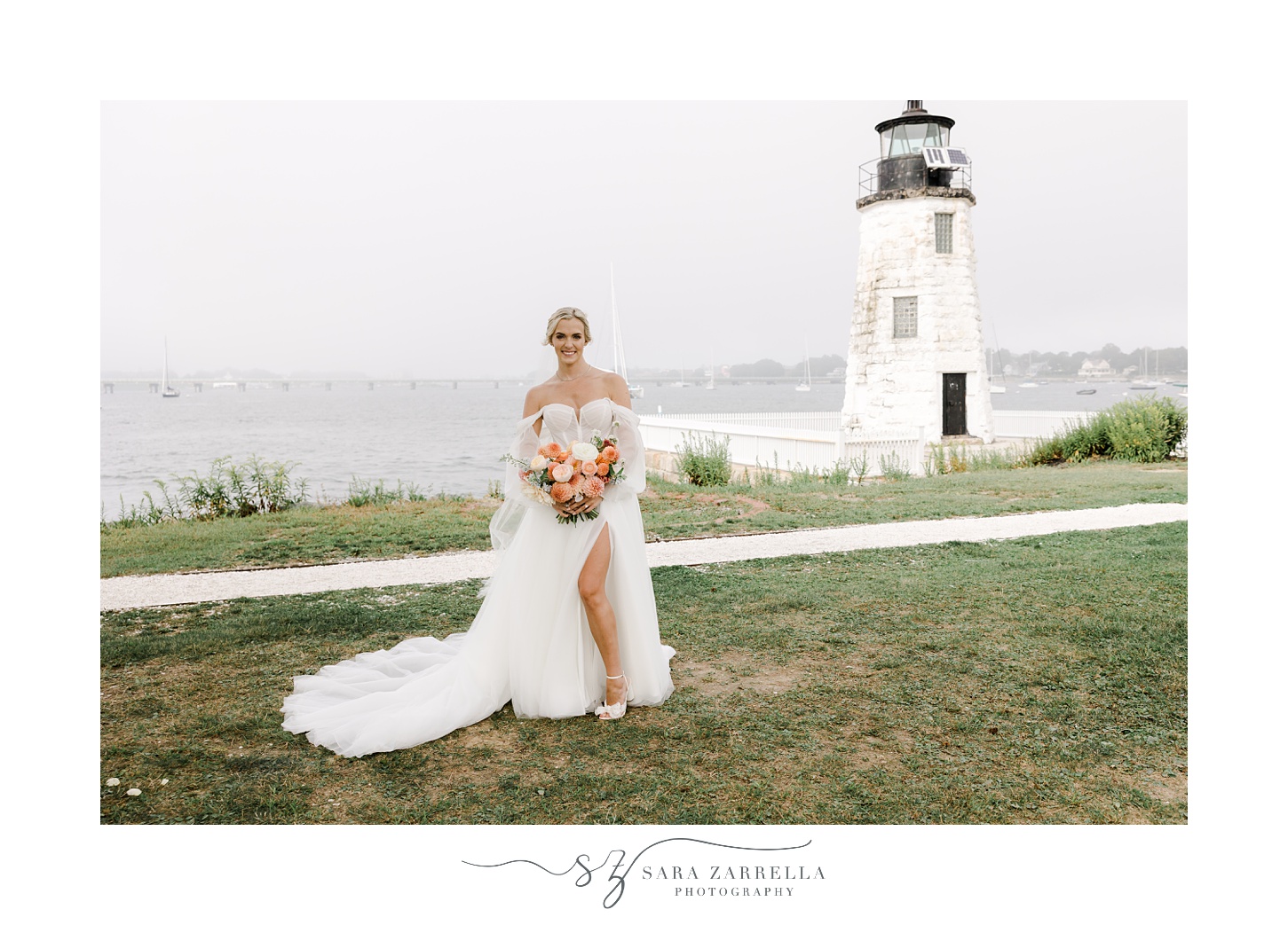 bride stands on lawn near the Newport Lighthouse with leg sticking out of wedding gown with peach and pink bouquet 