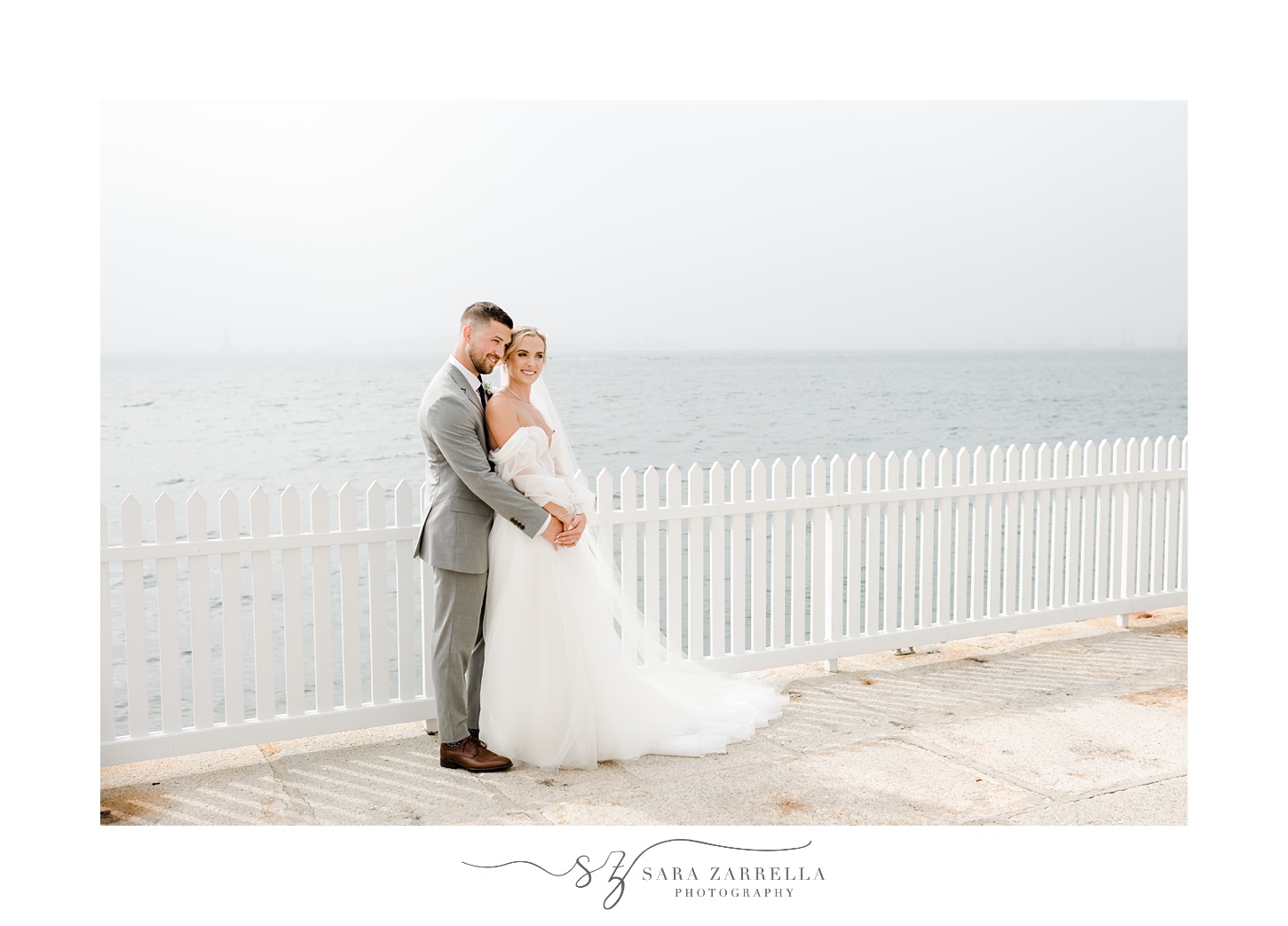 bride and groom kiss by white picket fence near Newport Lighthouse