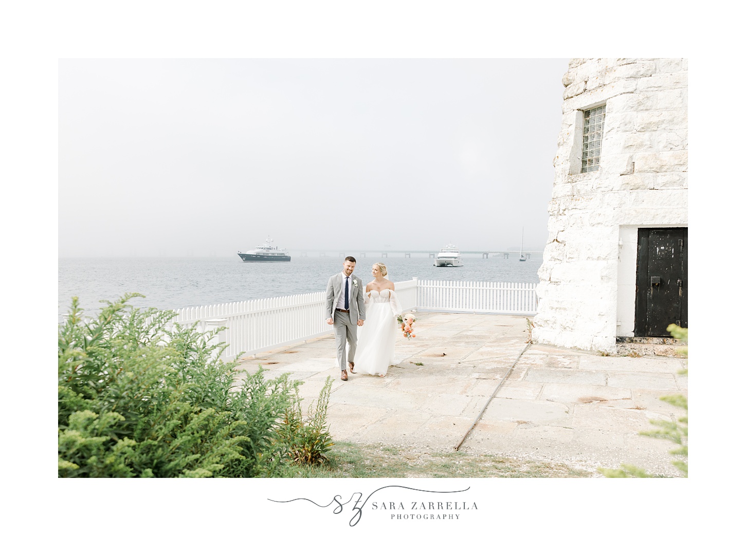 bride and groom walk along base of Newport Lighthouse 