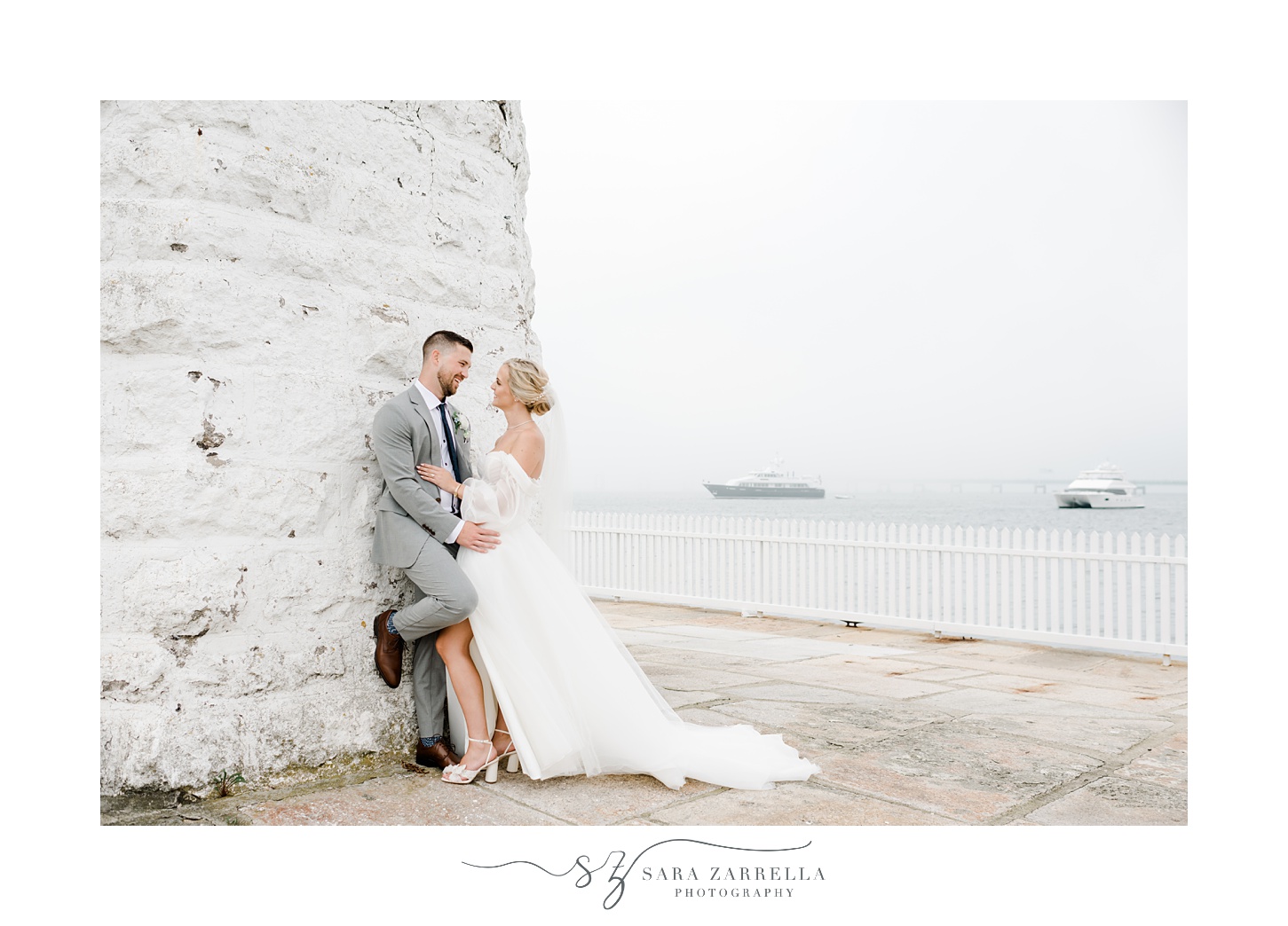 groom leans against Newport Lighthouse with wife next to him 