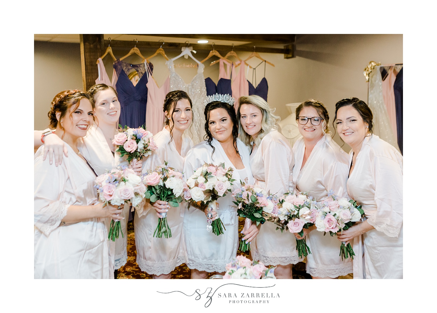bride poses with bridesmaids in matching robes holding pink and white flowers 