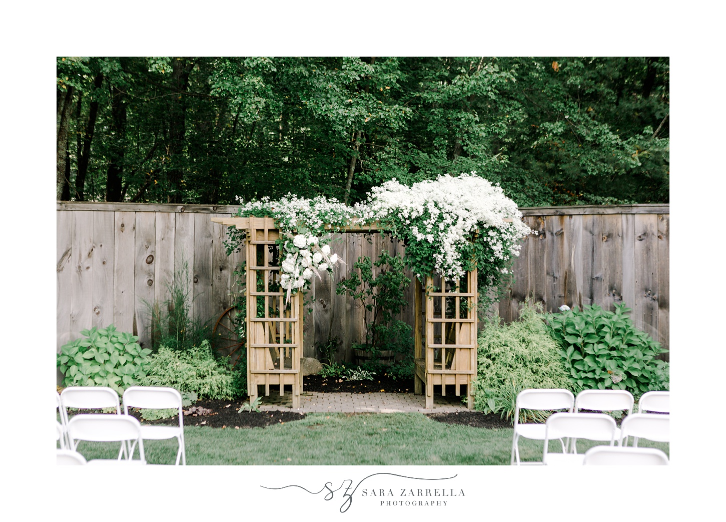 white flowers hang on wooden arbor at end of the aisle during Blissful Meadows wedding ceremony