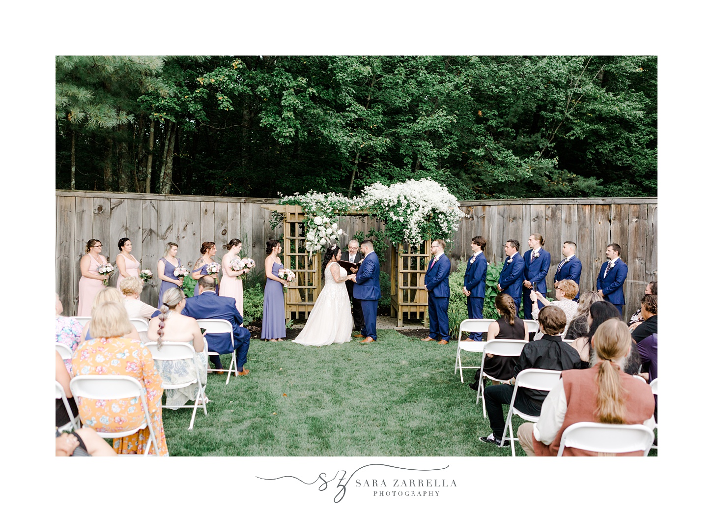 newlyweds exchange vows under wooden arbor with white flowers during Blissful Meadows wedding ceremony