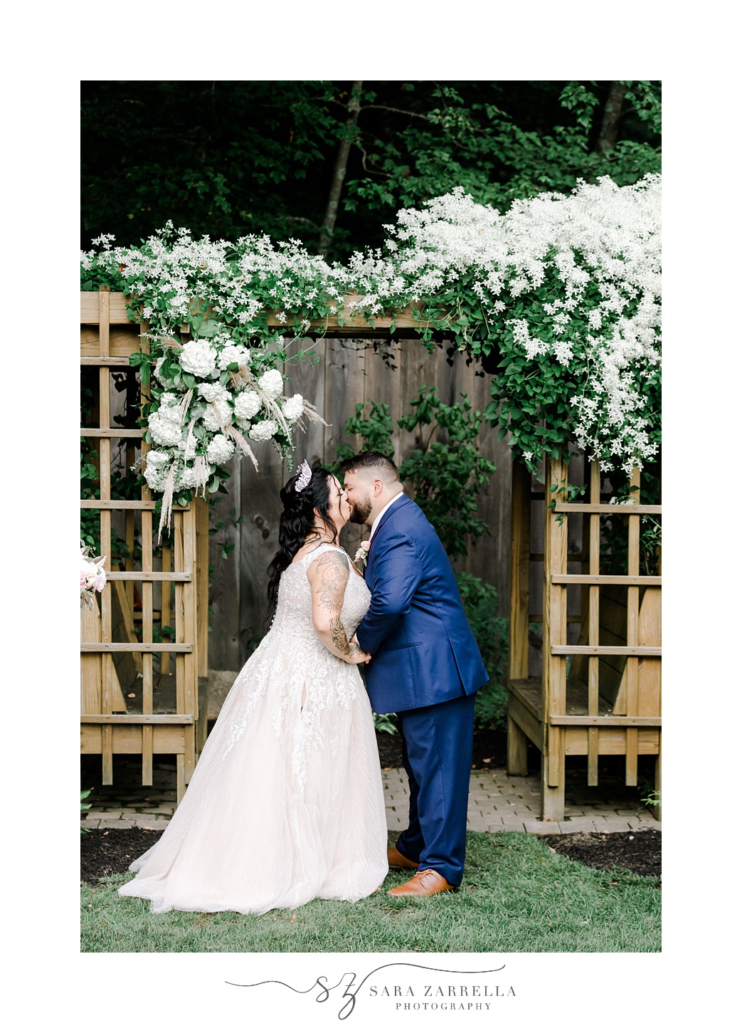 newlyweds kiss under wooden arbor with white flowers at Blissful Meadows wedding ceremony