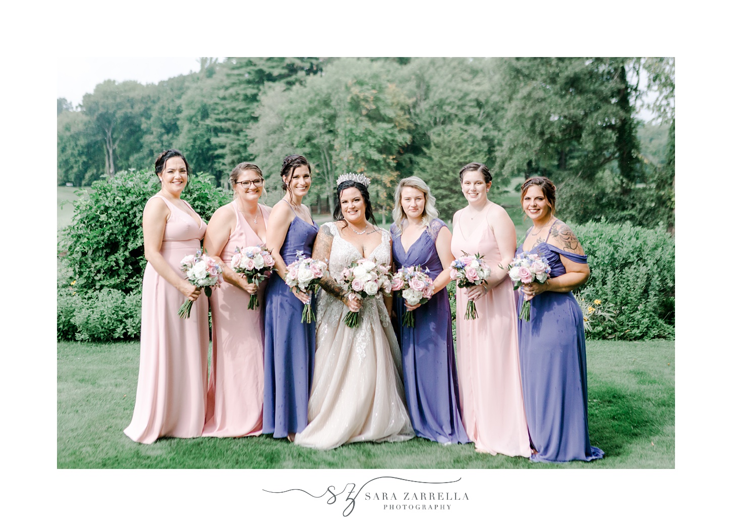 bride poses with bridesmaids in pink and purple gowns holding pink and white flowers 