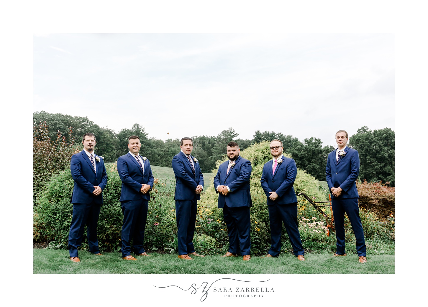 groom and groomsmen pose against wooden fence at Blissful Meadows