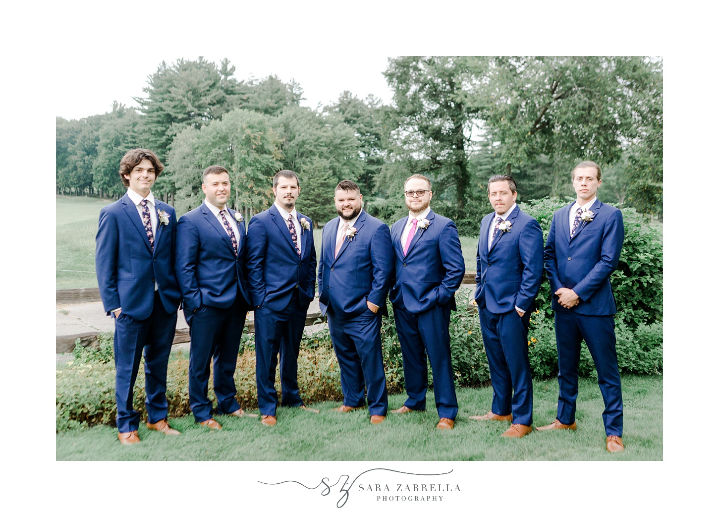 groom stands with groomsmen in navy suits with hands in pockets at Blissful Meadows