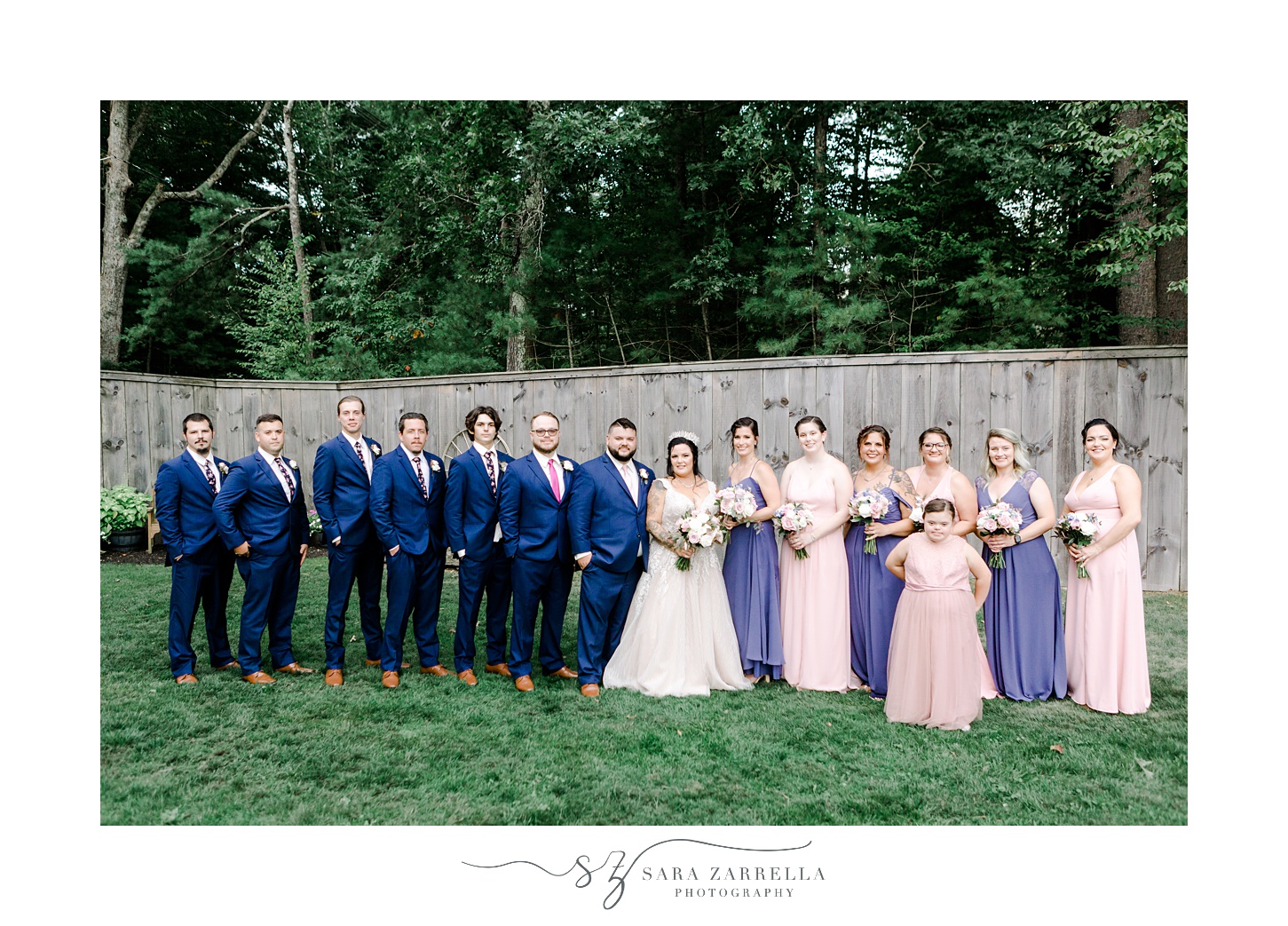 bride and groom pose with wedding party in front of wooden fence at Blissful Meadows