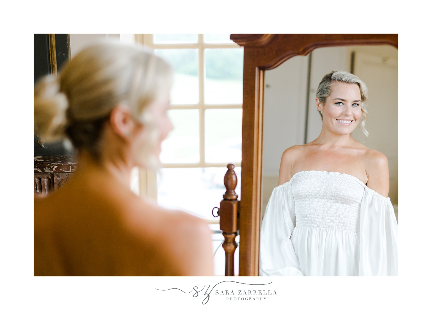 bride looks at herself in mirror in white off-the-shoulder gown
