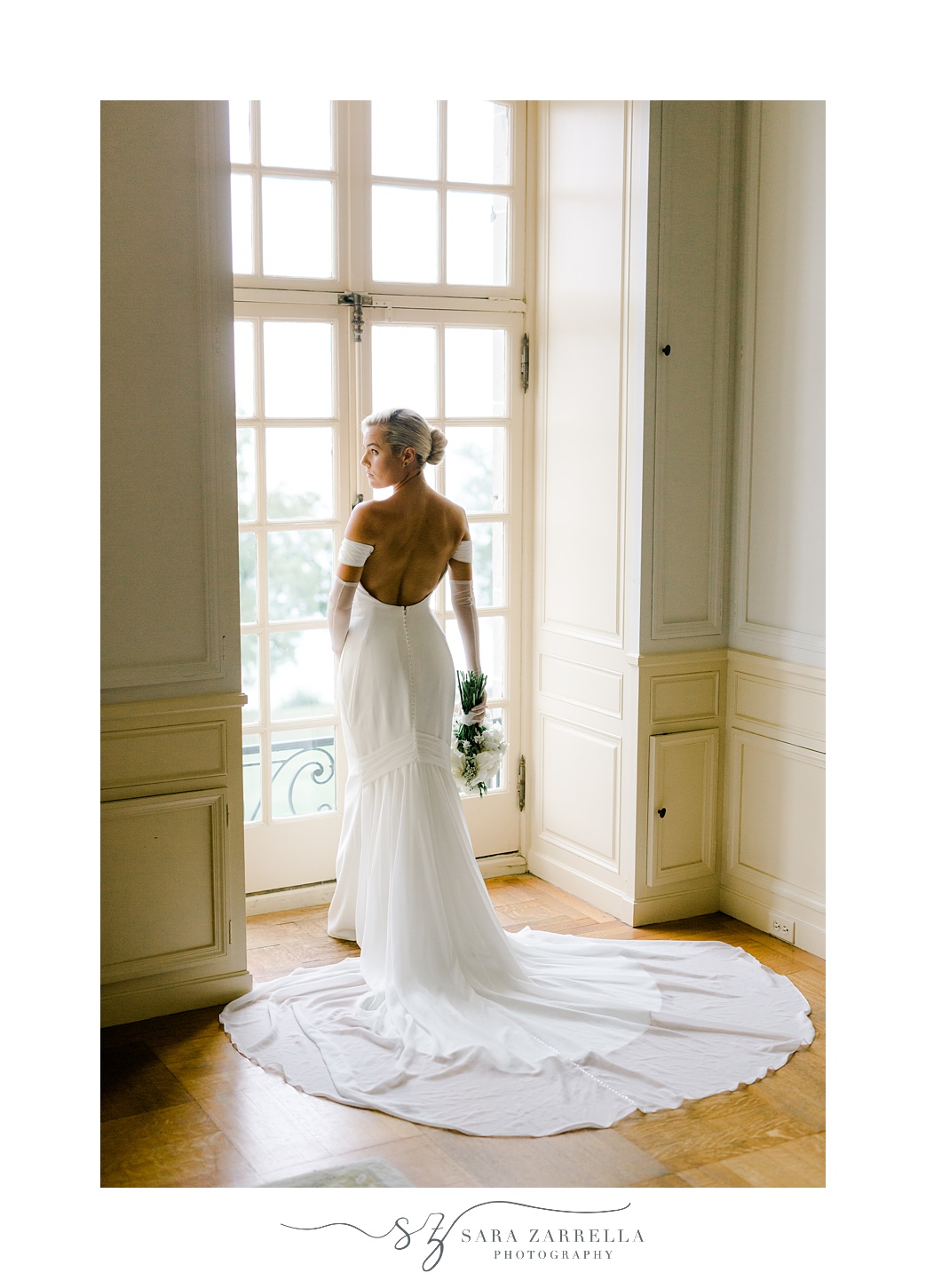 bride stands in window with bouquet of flowers and white gloves at Glen Manor House