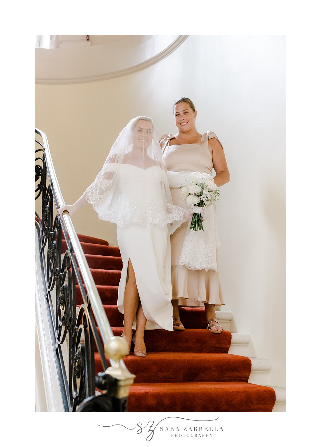 bride poses on steps inside Glen Manor House with sister 