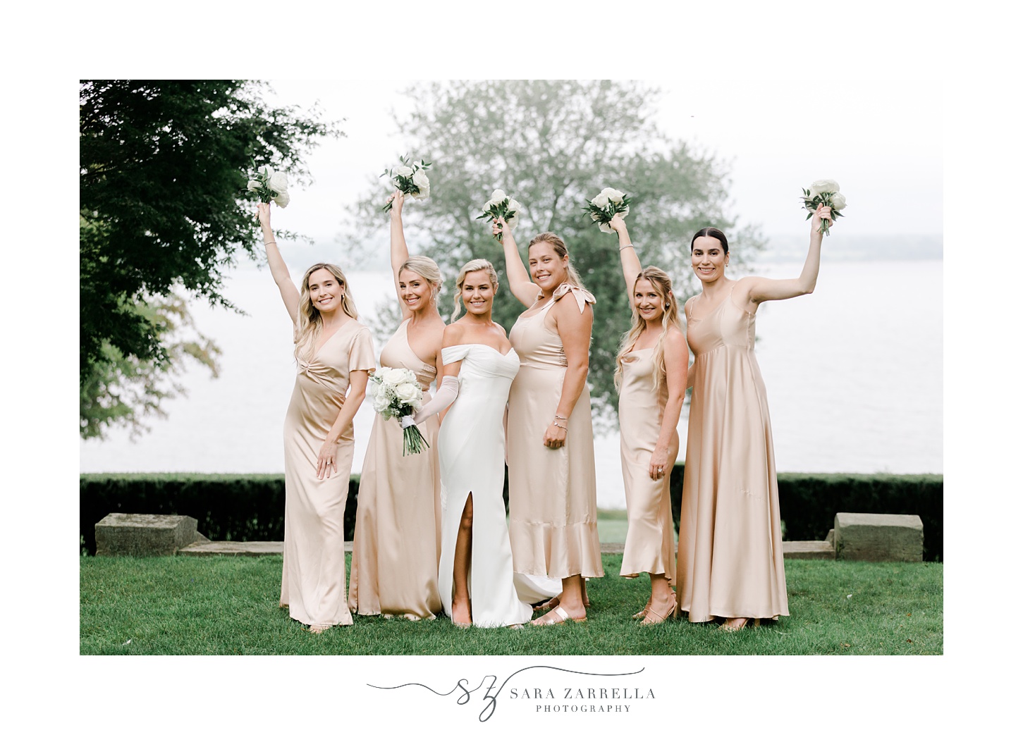 bride and bridesmaids cheer lifting up bouquets in front of water in Portsmouth RI