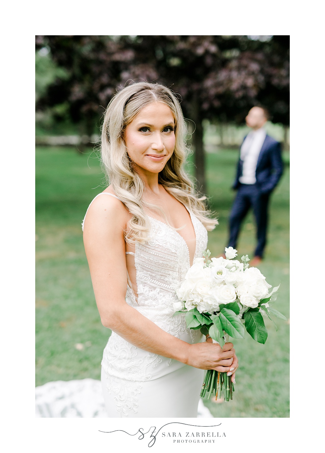 bride holds bouquet of white flowers inside Colt State Park with groom behind her