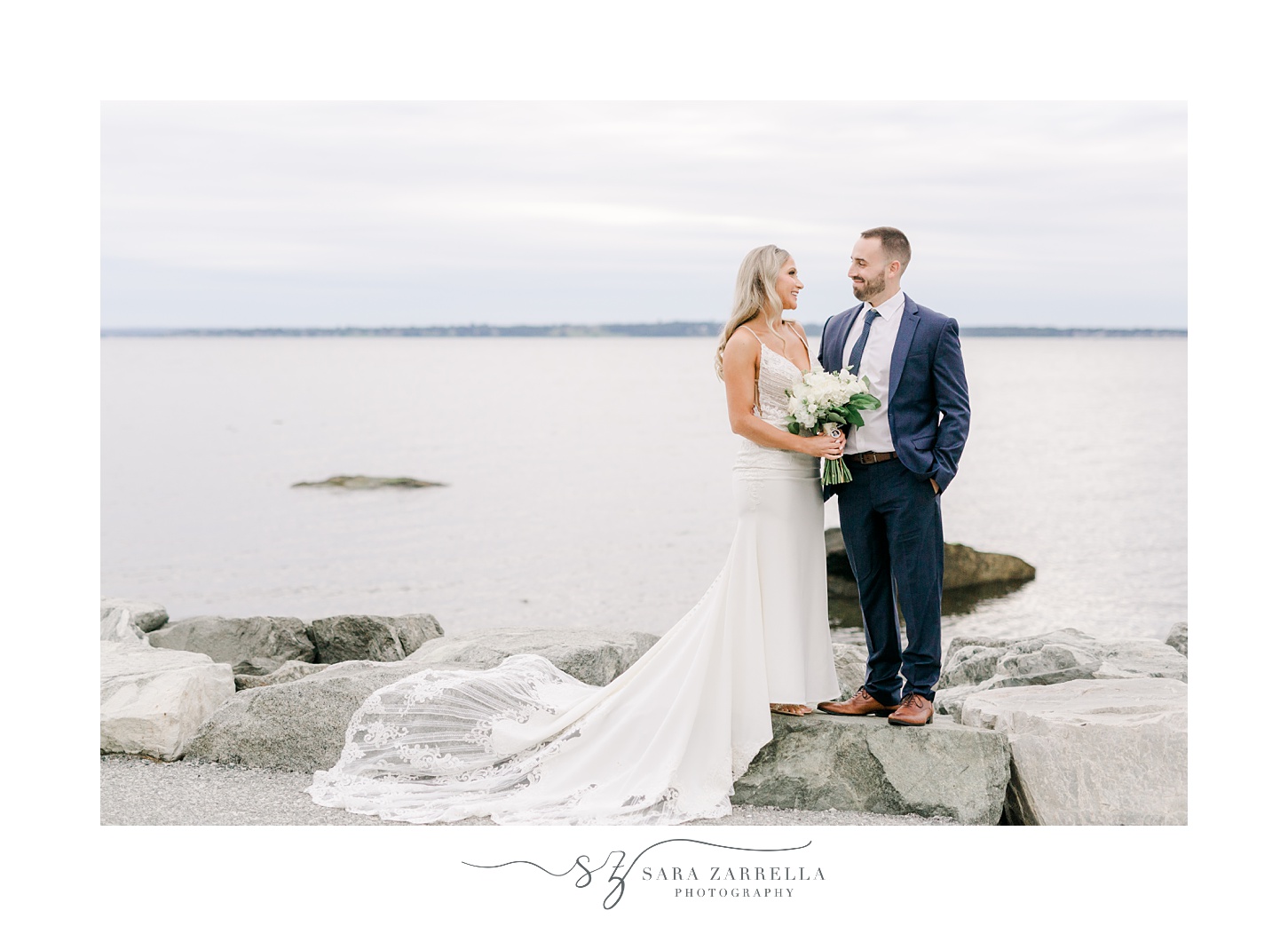 bride and groom pose on rocks in front of Narragansett Bay