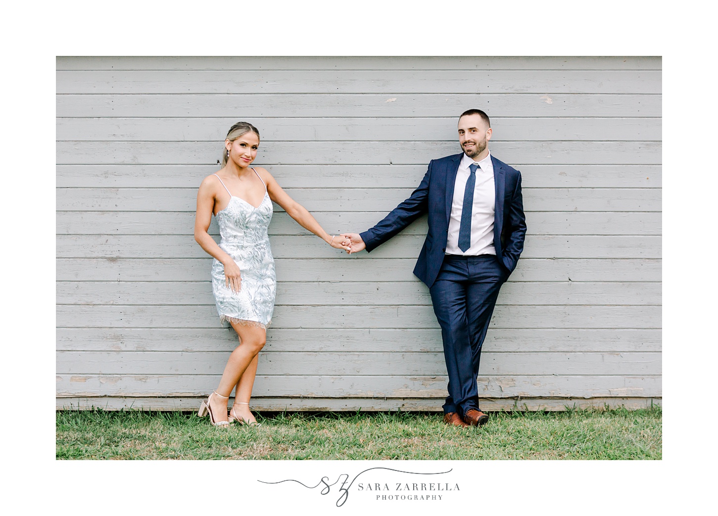 newlyweds hold hands leaning against grey wall of building at Colt State Park