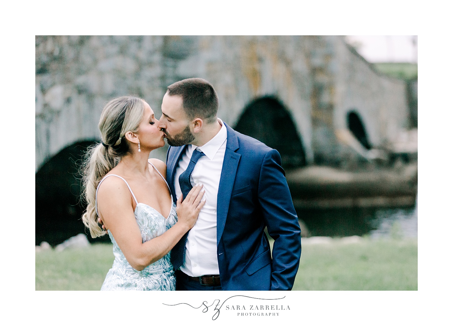 newlyweds lean to kiss near stone bridge inside Colt State Park