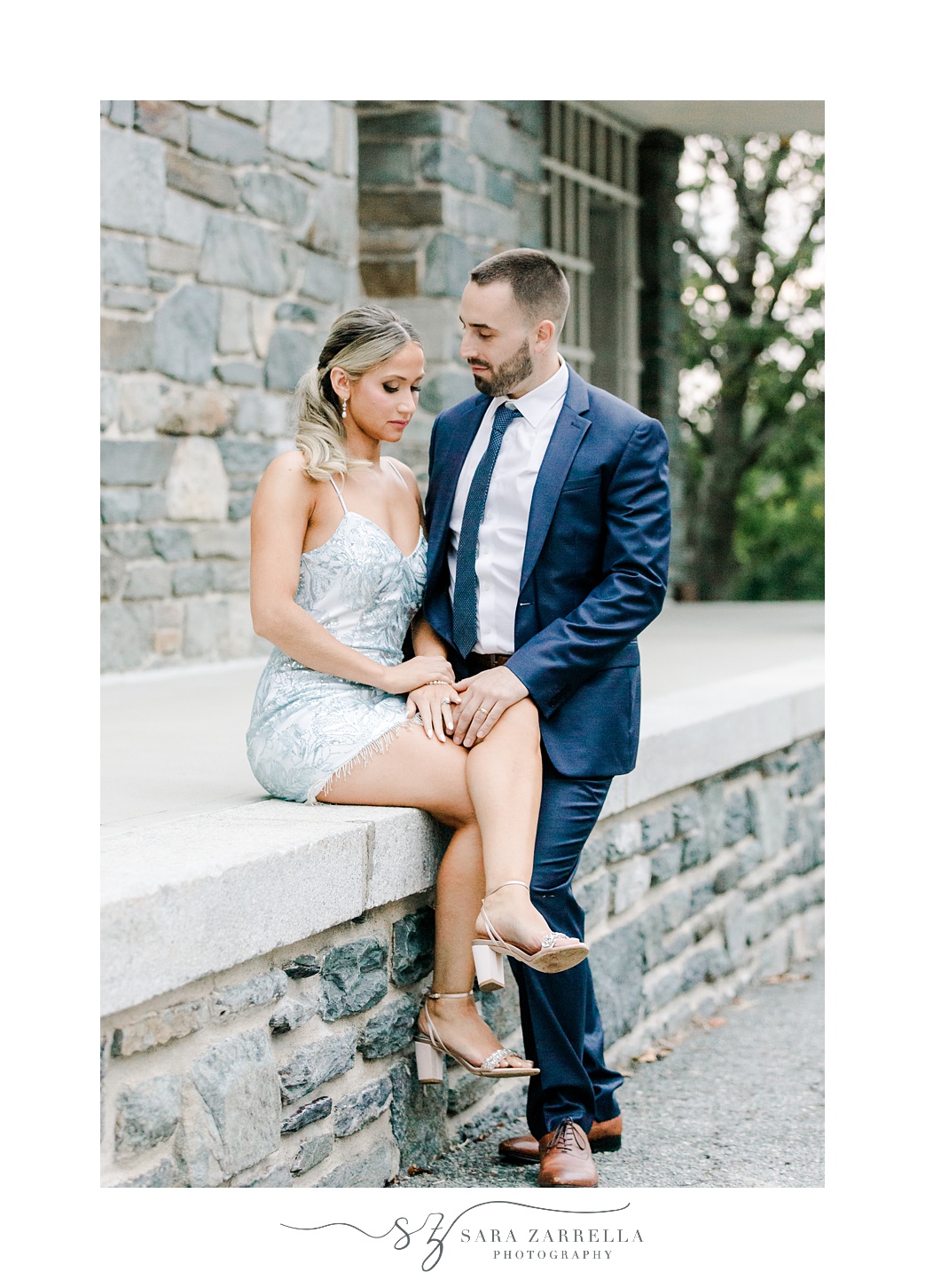 bride sits on stone wall inside Colt State Park with groom next to her 