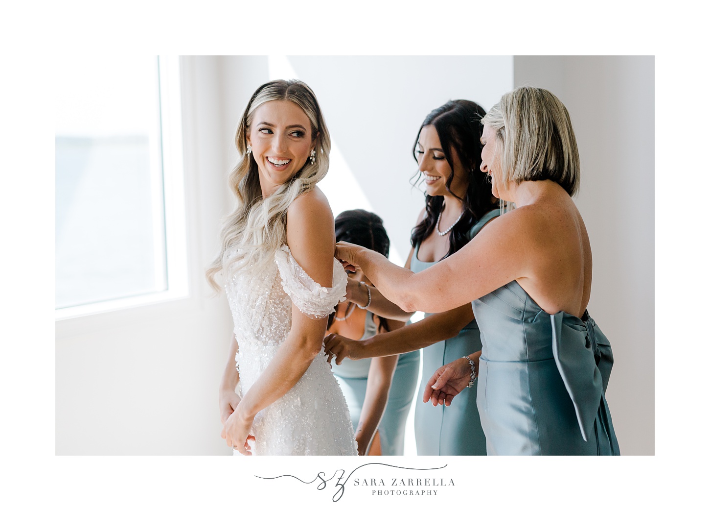 family helps bride into wedding dress before Belle Mer Island House wedding