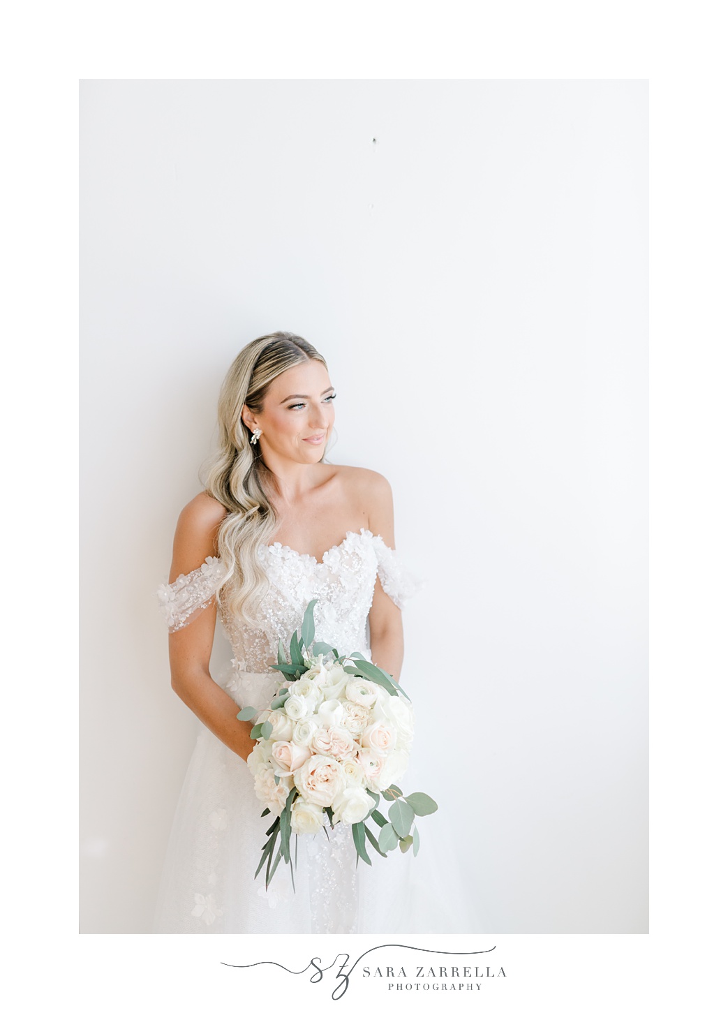 bride poses in off-the-shoulder wedding gown with pastel pink and white bouquet 
