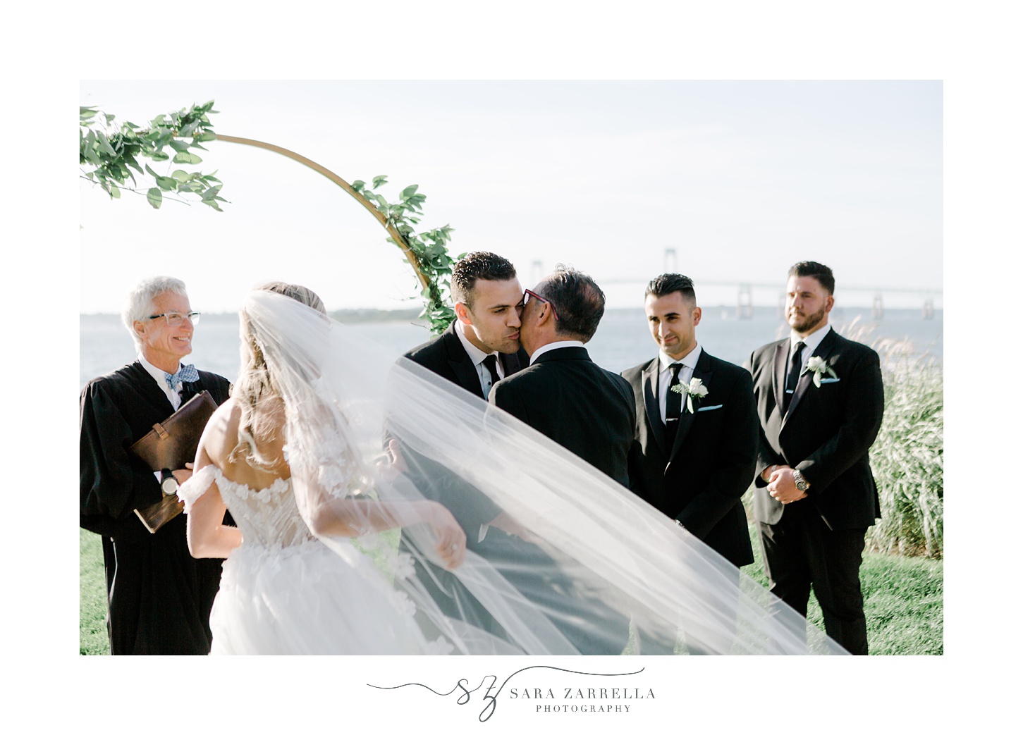 groom hugs bride's father during waterfront wedding ceremony on lawn at Belle Mer Island House