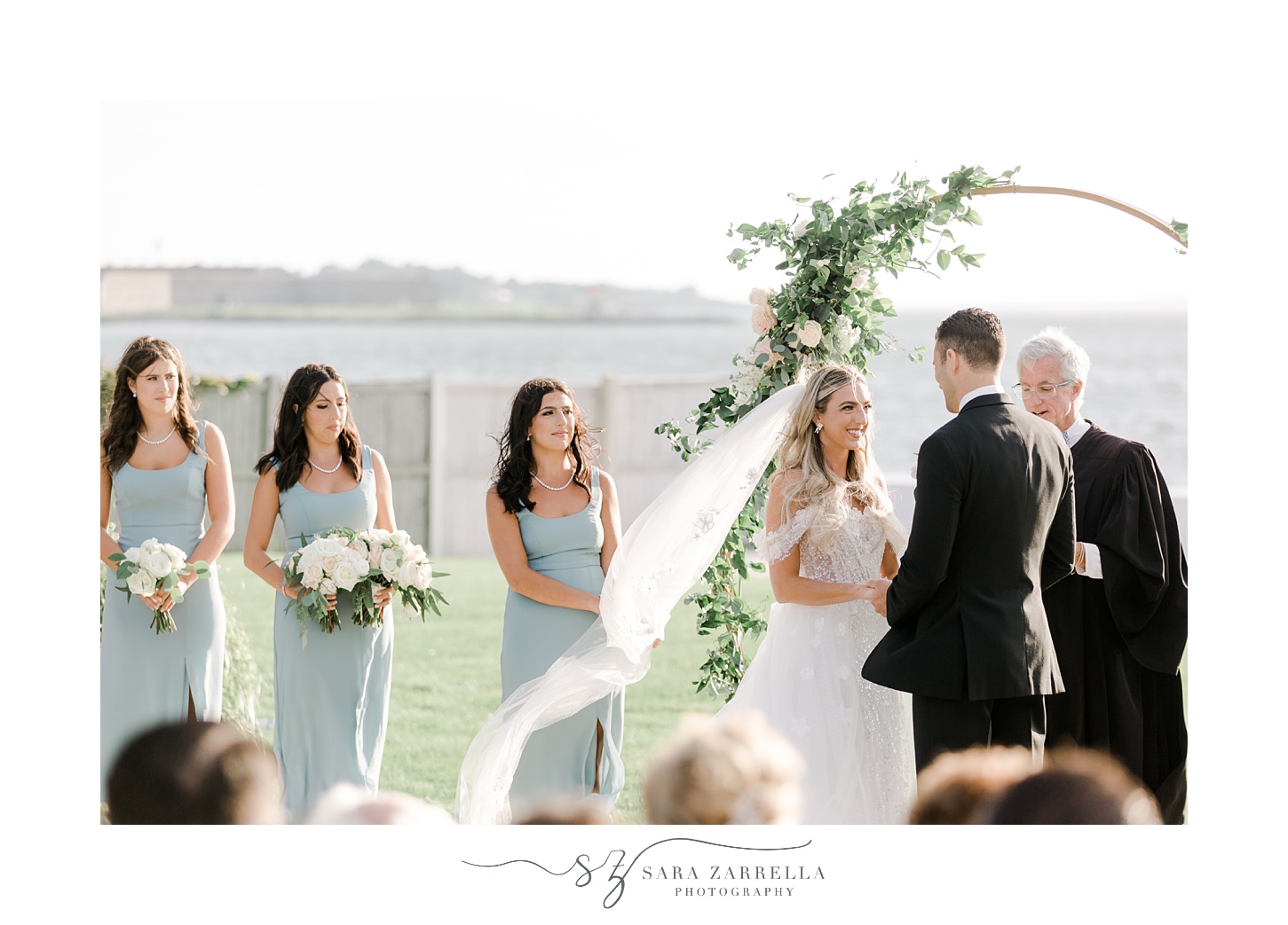 bride looks at groom during waterfront wedding ceremony on lawn at Belle Mer Island House