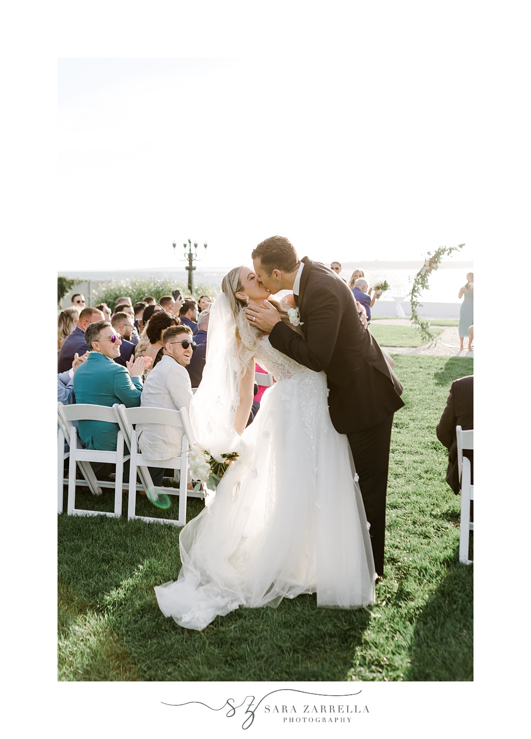 groom kisses bride in aisle after waterfront wedding ceremony on lawn at Belle Mer Island House