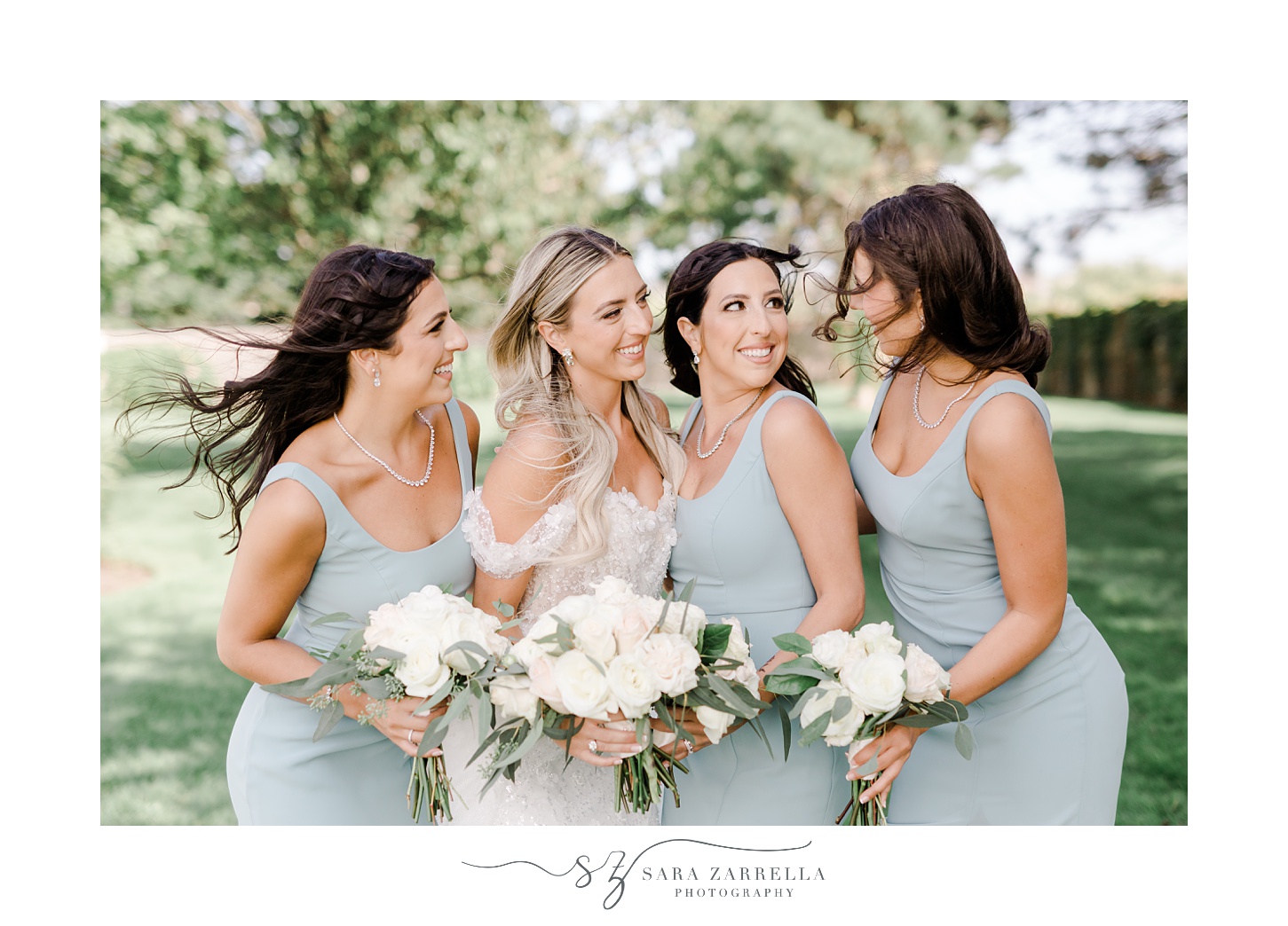 bride and three bridesmaids in light blue dresses smile at her during summer wedding day