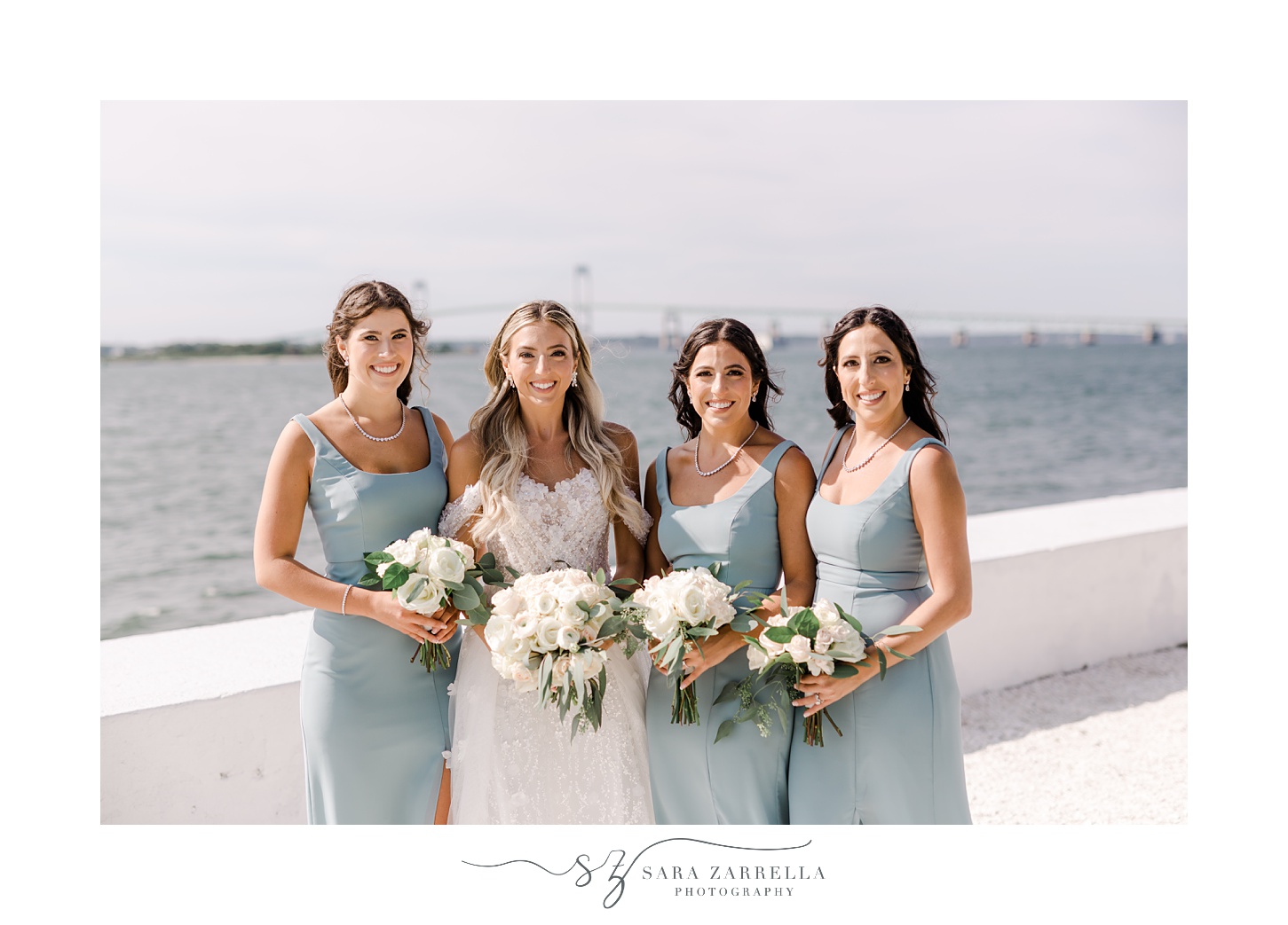 bride and bridesmaids hold bouquets of white flowers in front of bay in Newport RI