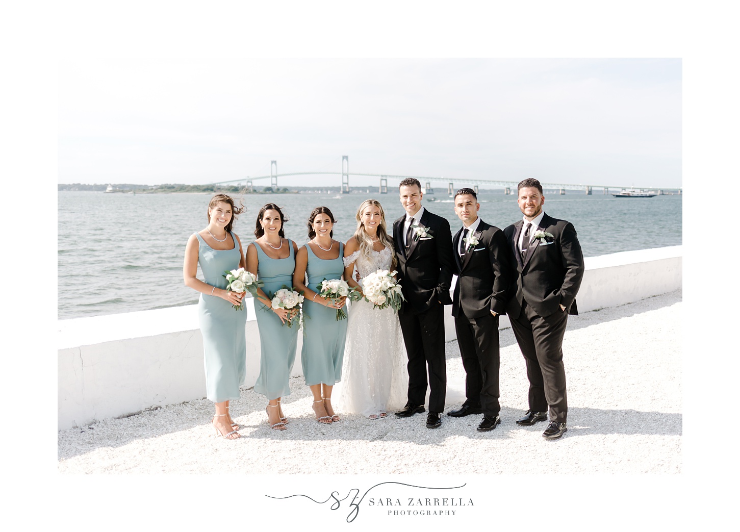 bride and grooms stand with 6 person wedding party in front of white wall at Belle Mer Island House