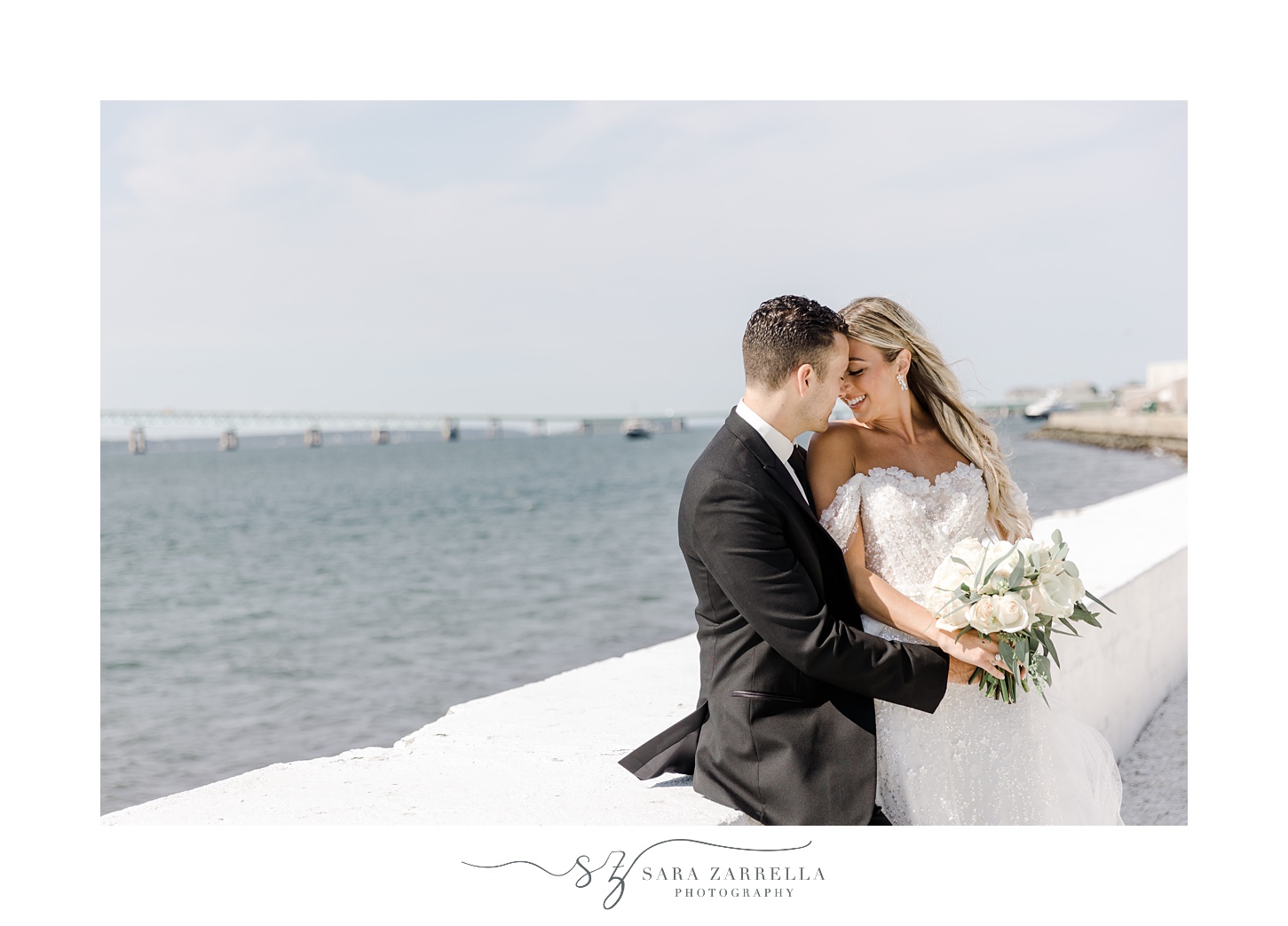 bride and groom lean heads together and lean against white wall in Newport RI
