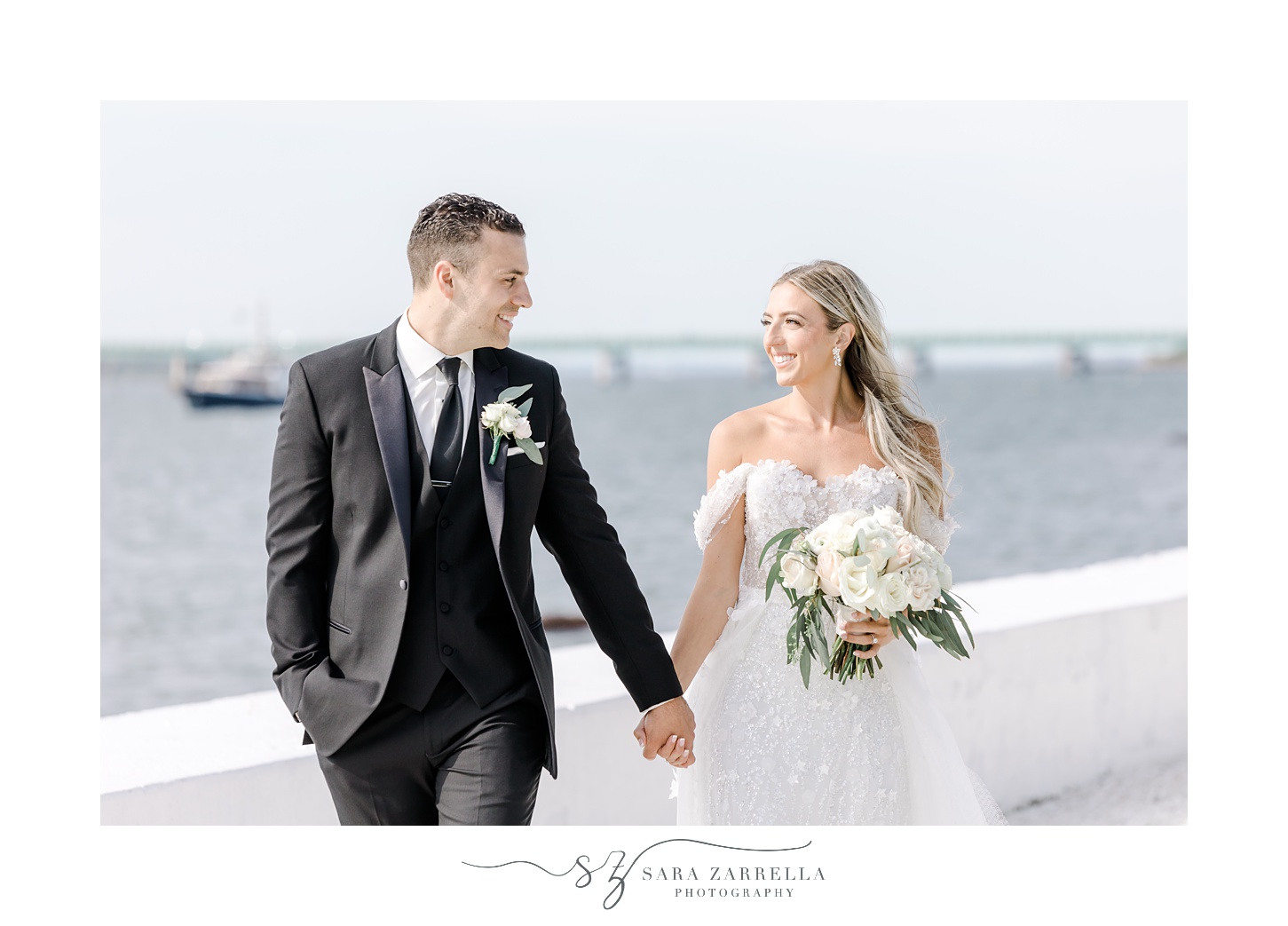 bride and groom hold hands near white wall of Belle Mer Island House