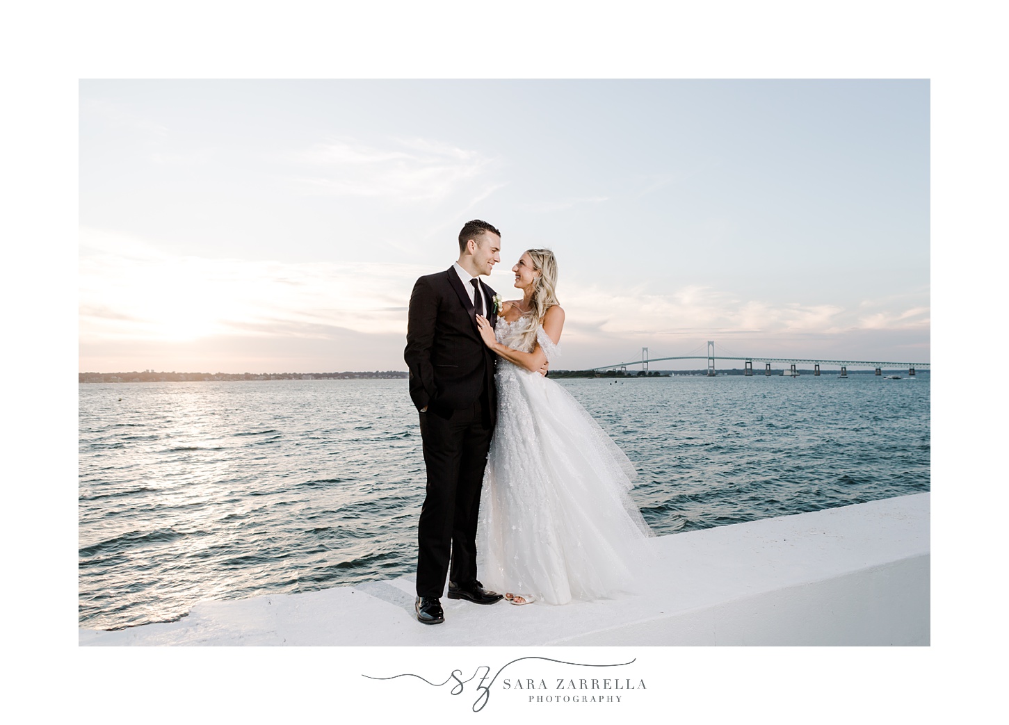 bride and groom stand on white wall outside Belle Mer Island House
