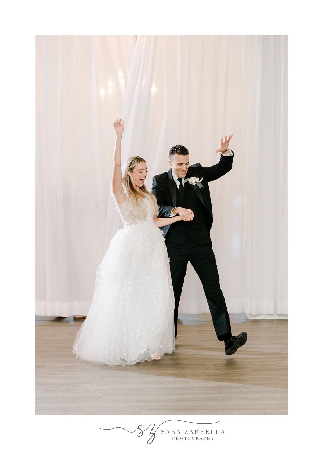 bride and groom cheer walking into reception in front of white wall 