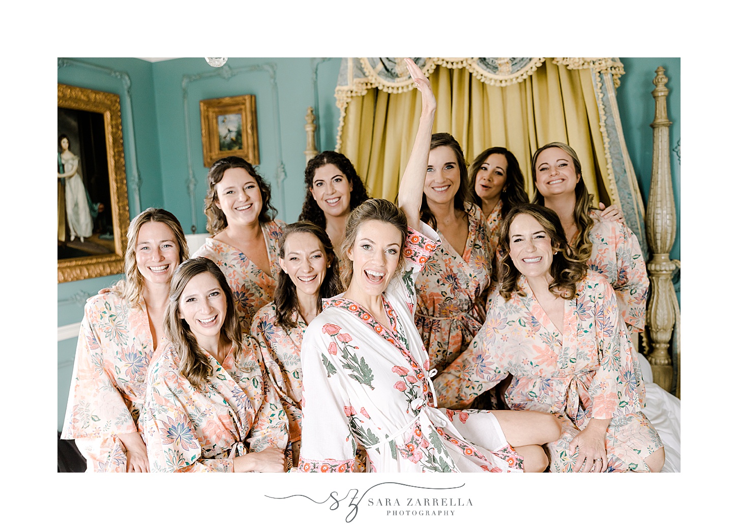 bride sits on bed with bridesmaids in pink robes inside the bridal suite at the Chanler