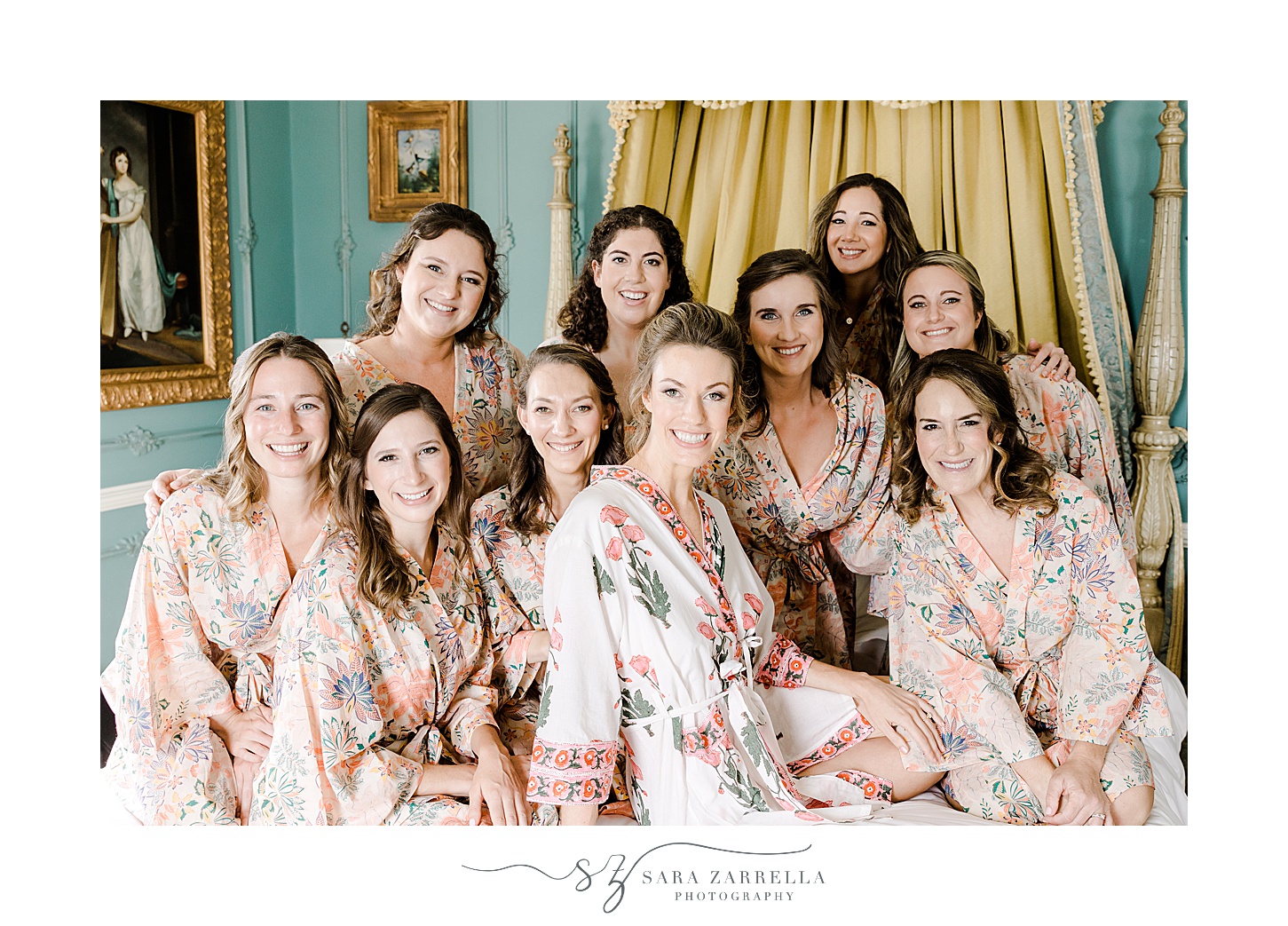 bride sits with bridesmaids in pink robes on bed inside the bridal suite at the Chanler