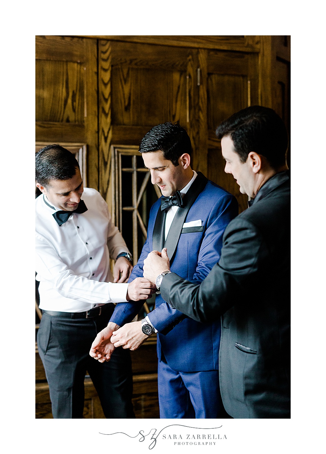 groomsmen help groom into blue suit jacket with black lapels at the Chanler