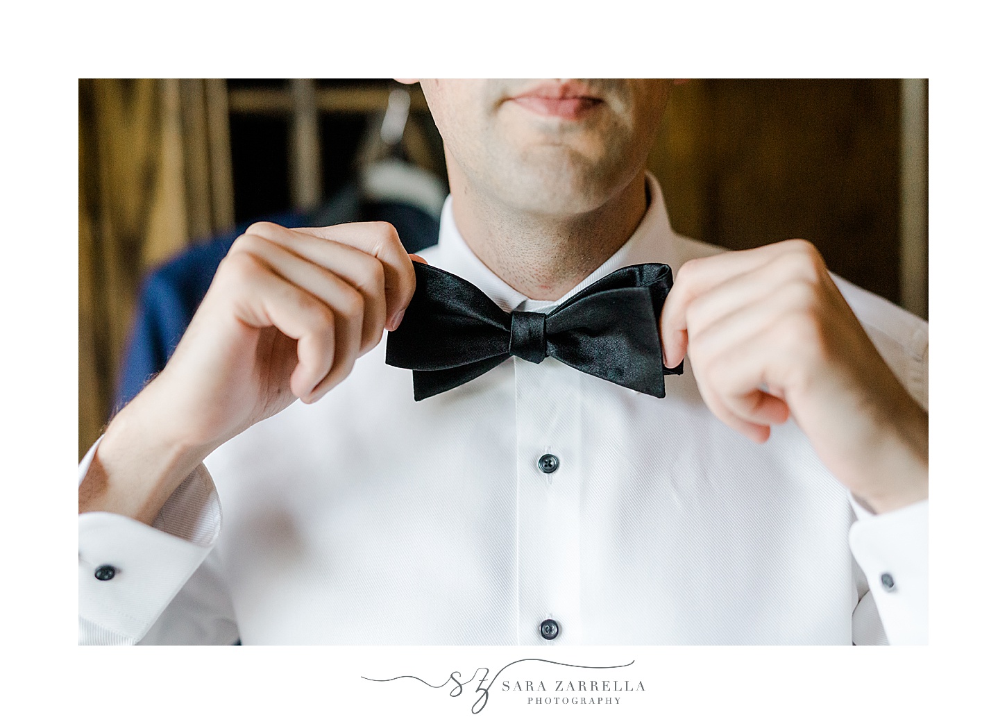 groom adjusts black bow tie before wedding at the Chanler