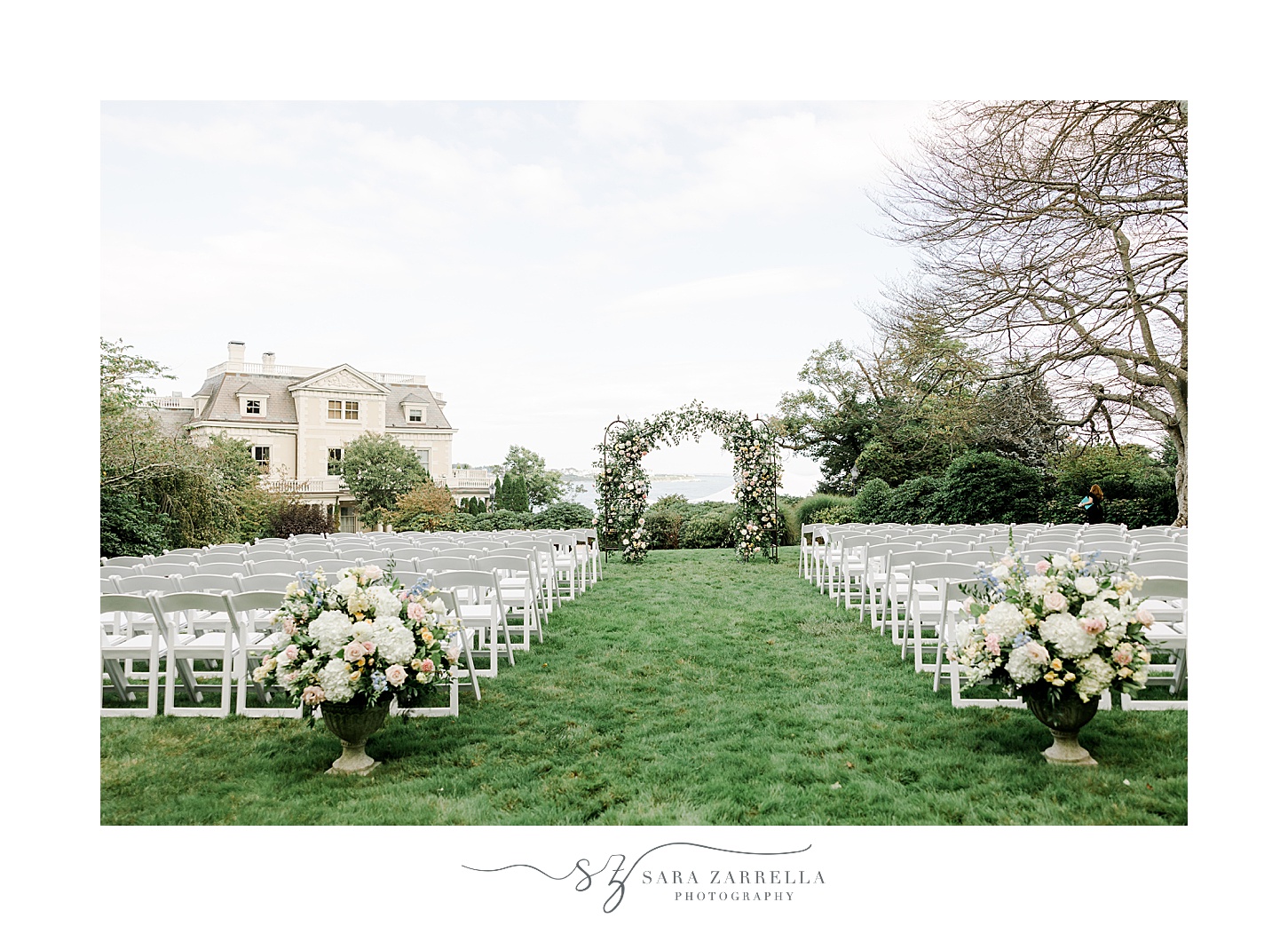 wedding ceremony on lawn at the Chanler with white chairs and greenery covered arbor 
