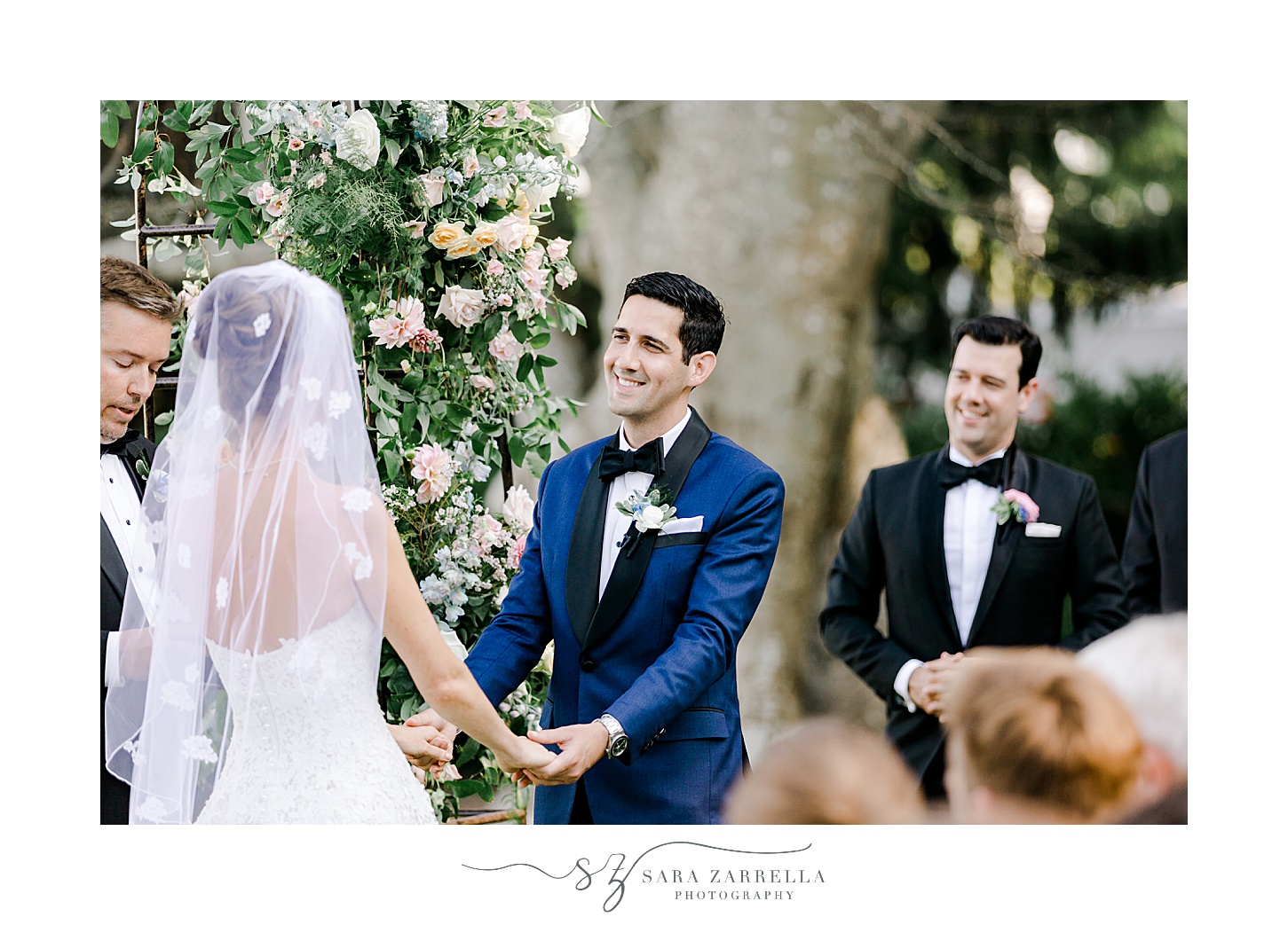 groom grins at bride holding her hands during ceremony on lawn at the Chanler