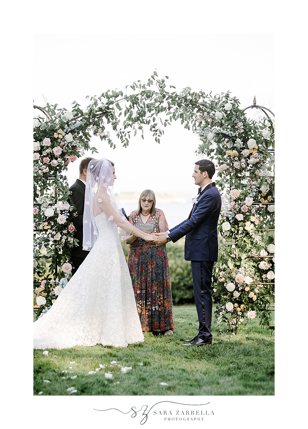 newlyweds hold hands in front of arbor covered in flowers at the Chanler